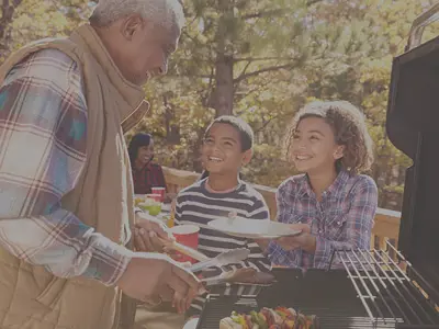 man barbecuing food with kids holding out plates